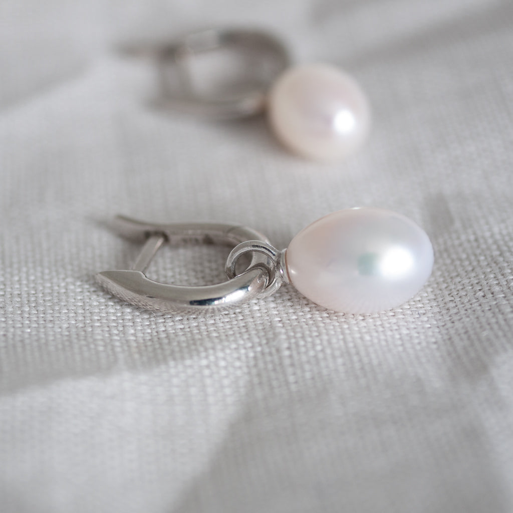 Pearl earring with silver hook on a light fabric background
