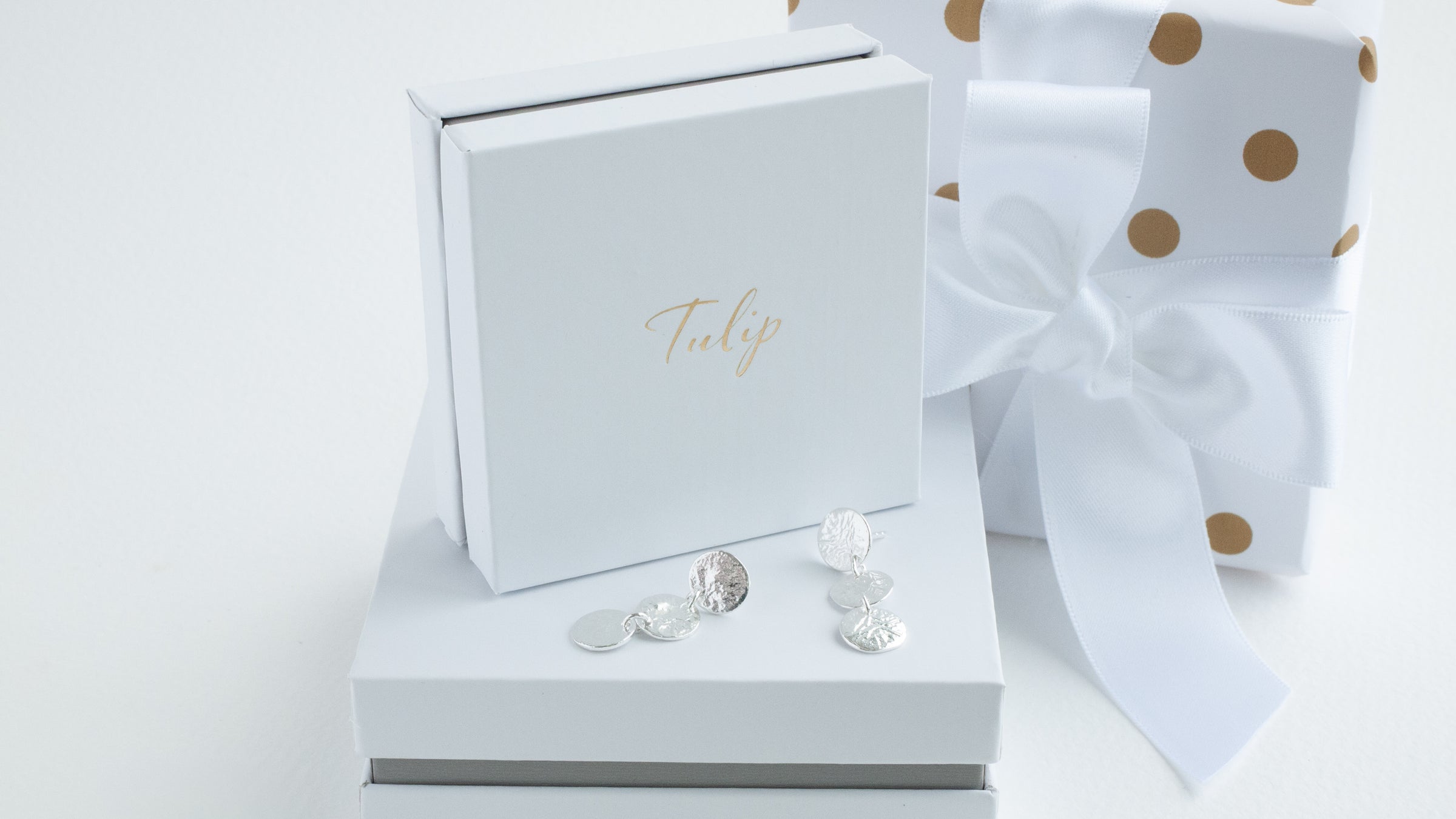 Silver earrings on a white jewelry box with a polka dot bow