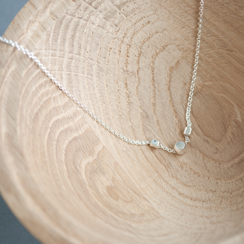 Silver necklace with small cube pendants on a wooden surface